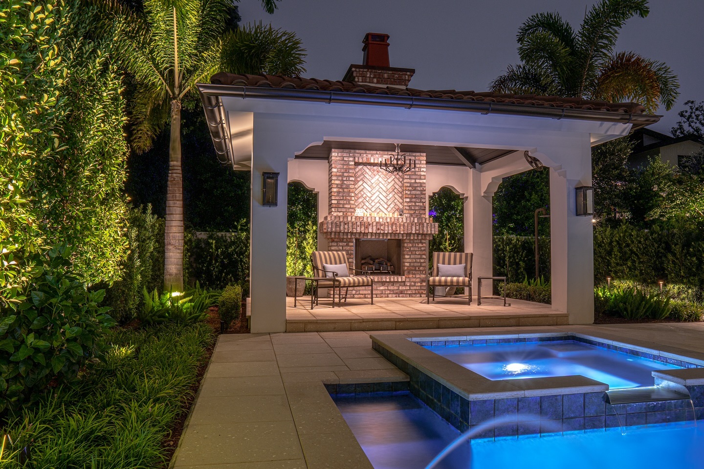 Outdoor cabana with brick herringbone fireplace and spa at night