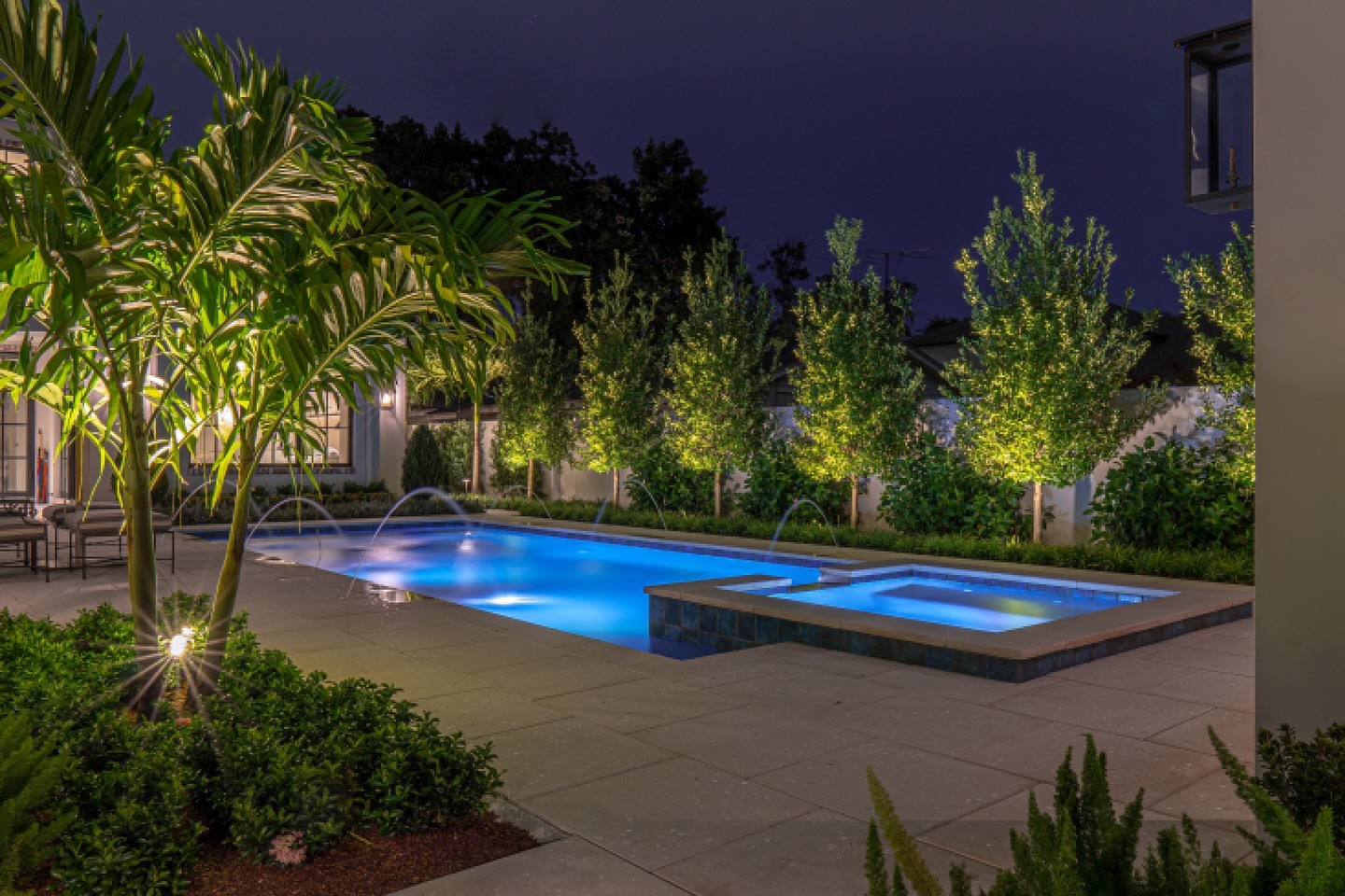 Nighttime pool and spa with water features and landscape lighting