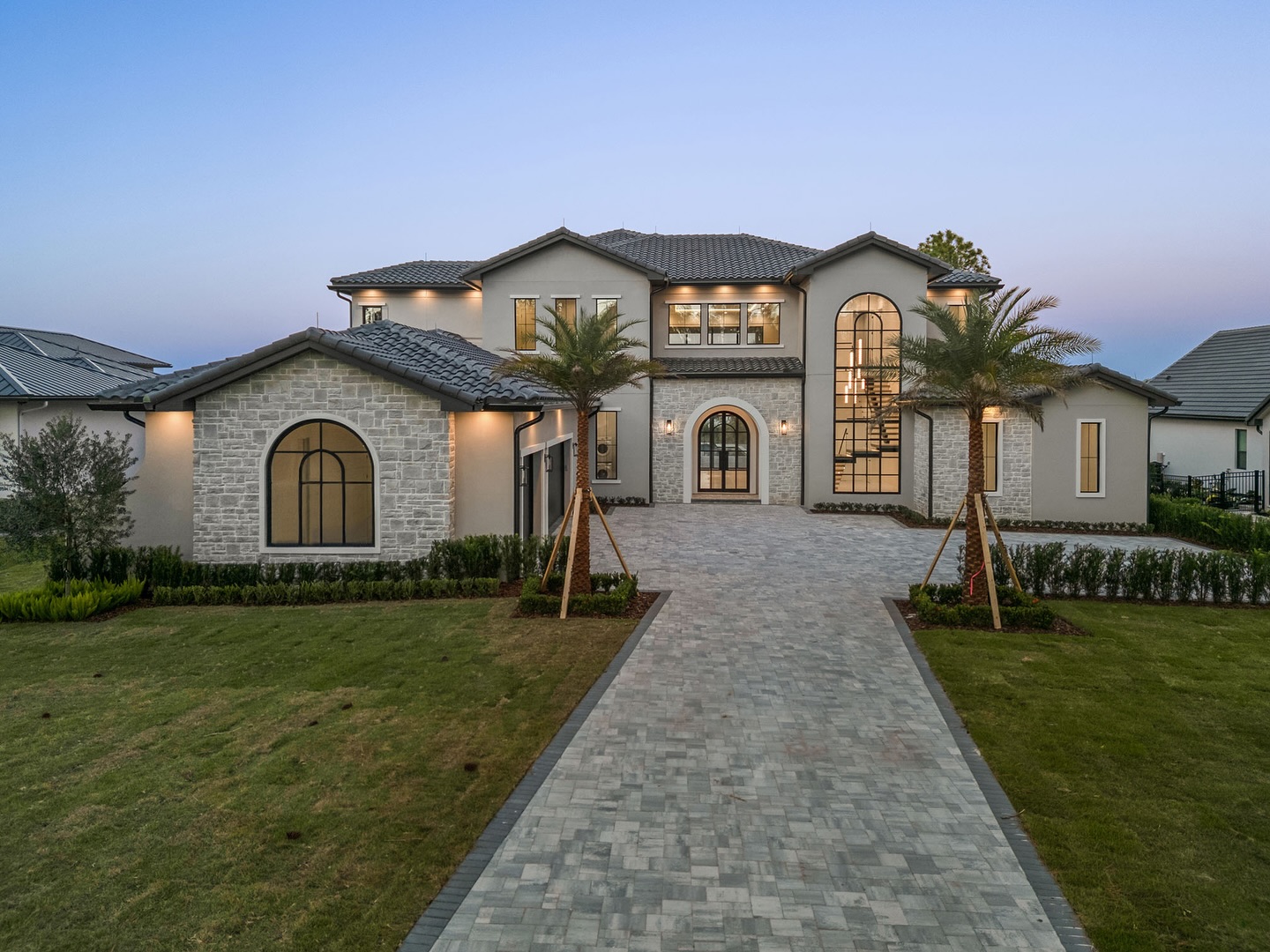 Grand stone home with paver driveway and front landscape